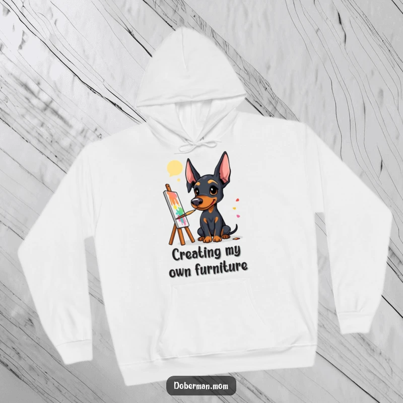 Funny Doberman artist hoodie showing a dog with a paintbrush at a canvas, creating a vibrant and colorful masterpiece.